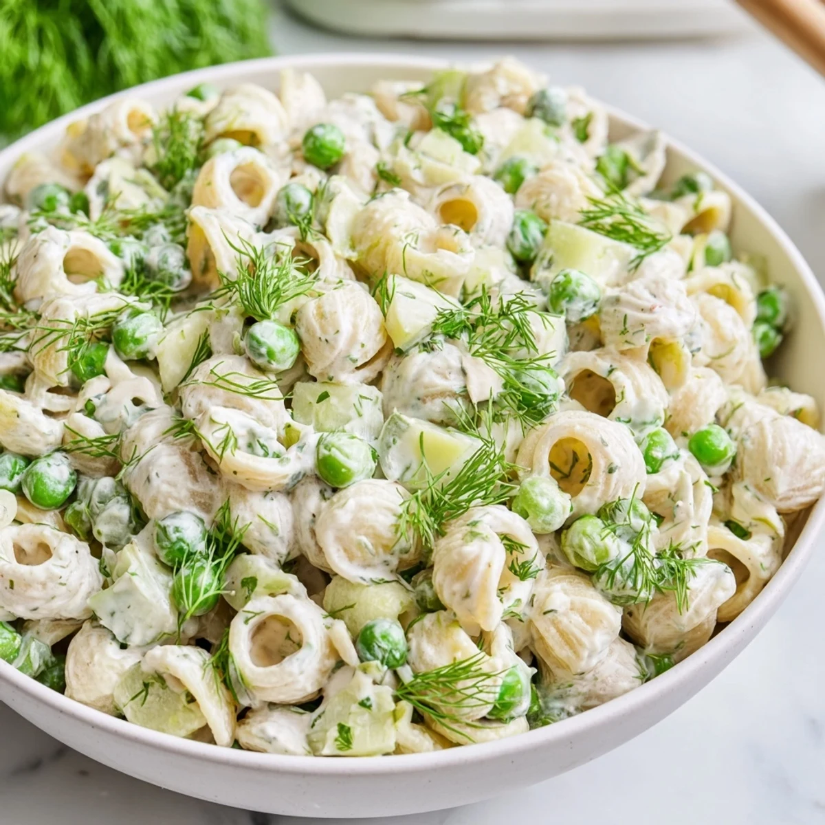 Creamy Dill Pickle Pasta Salad served in a white bowl with ditalini, green peas, and diced pickles on a rustic wooden table.