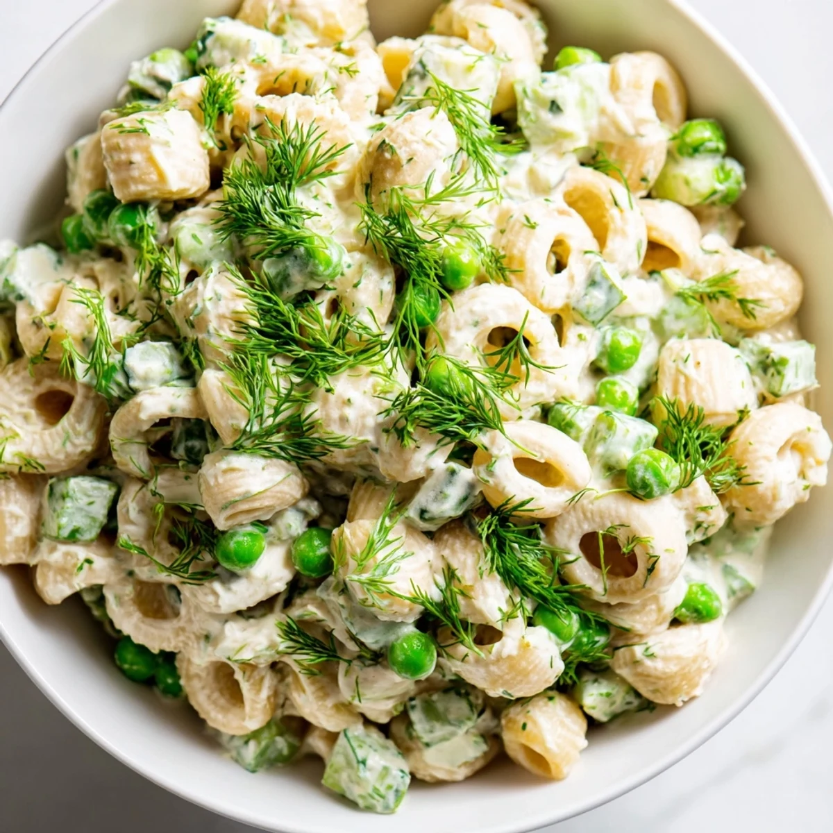 A close-up of Creamy Dill Pickle Pasta Salad showing a creamy dressing coating the pasta, pickles, and fresh dill garnish.