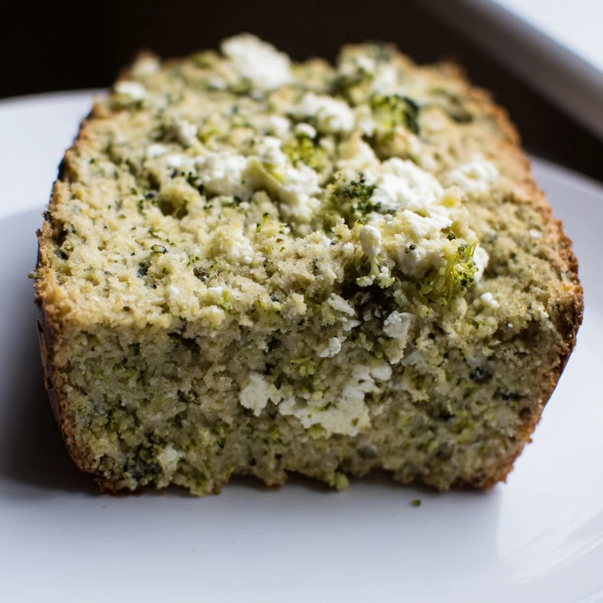 A slice of moist broccoli and feta loaf showing tender green florets and creamy crumbles, perfect for a savory snack.  