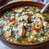 Steaming bowl of Greek Chicken & Pearl Couscous Soup topped with feta and fresh dill.