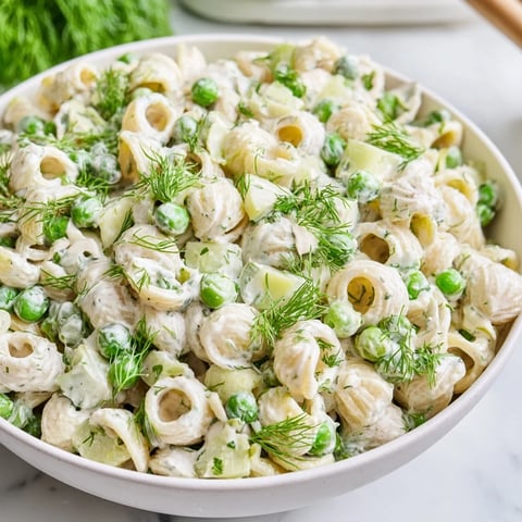 Creamy Dill Pickle Pasta Salad served in a white bowl with ditalini, green peas, and diced pickles on a rustic wooden table.