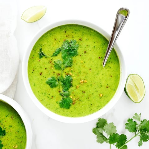 A bowl of vibrant Spinach Coriander Lemongrass Soup garnished with fresh cilantro leaves and a lime wedge.  