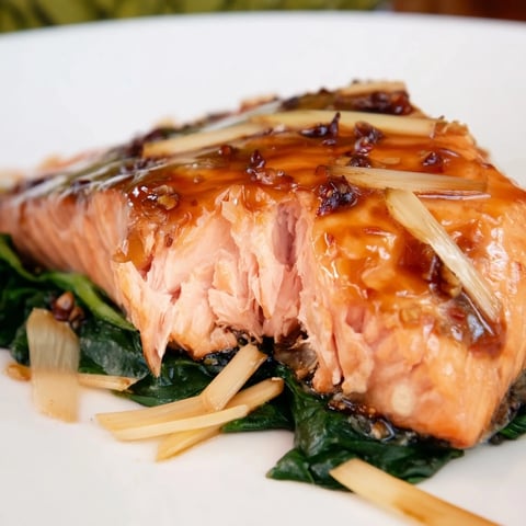 Golden-brown miso salmon fillets glazed with sweet umami sauce, resting on tender sautéed spinach with fresh ginger, served with lemon wedges.