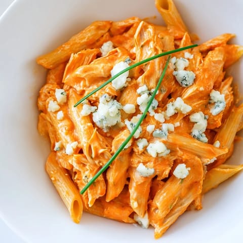 A hearty skillet of Buffalo Chicken Pasta tossed with tender shredded chicken in a vibrant, spicy orange sauce.  