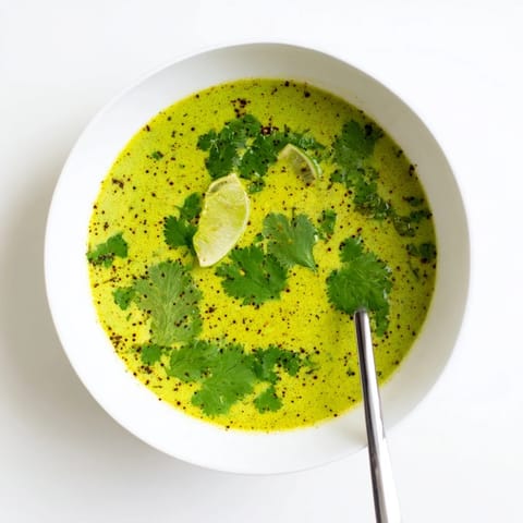 Steaming creamy Spinach Coriander Lemongrass Soup in a rustic white bowl with a spoon beside it.  