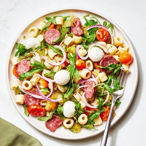 Freshly tossed Spring Antipasto Pasta Salad featuring salami, pickled giardiniera vegetables, and cherry tomatoes in a zesty dressing.