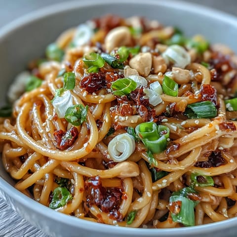 Spicy chili crisp noodles in a savory sauce, topped with crunchy scallions and peanuts for a satisfying Asian-inspired meal.  