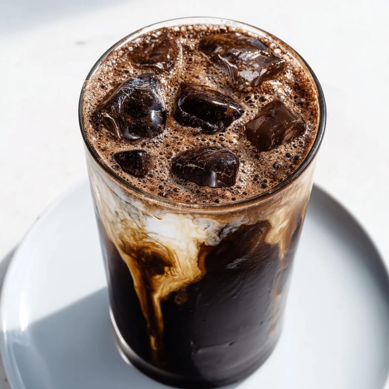 Glistening chocolate cracking iced latte, showcasing a decadent topping over icy milk and coffee for a sweet treat.