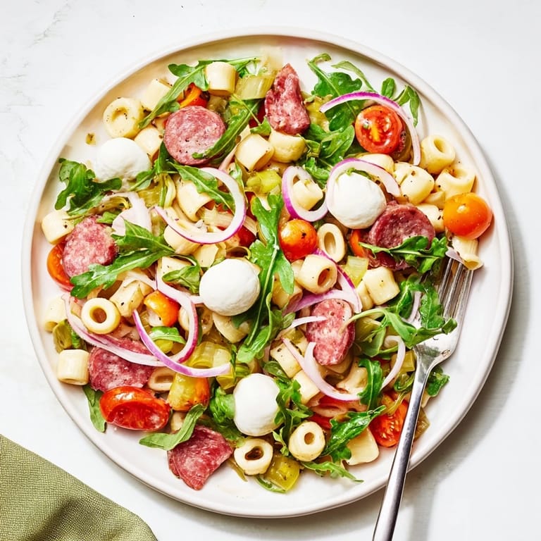 Freshly tossed Spring Antipasto Pasta Salad featuring salami, pickled giardiniera vegetables, and cherry tomatoes in a zesty dressing.